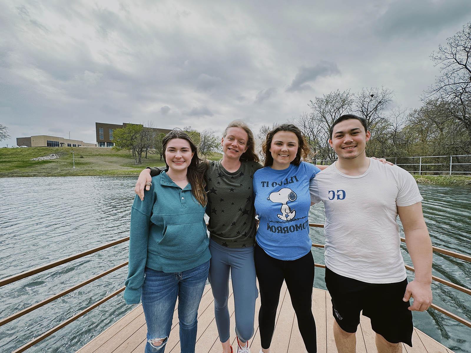 Four students with arms over shoulders standing in front of pond